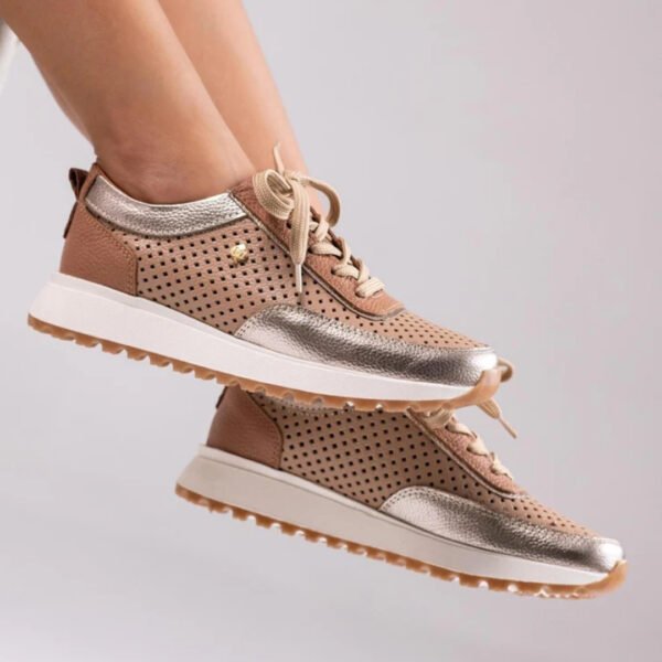 Tenis casuales para mujer en color beige (nude) y detalles metálicos dorados. El diseño presenta perforaciones y suela blanca con bordes de goma.