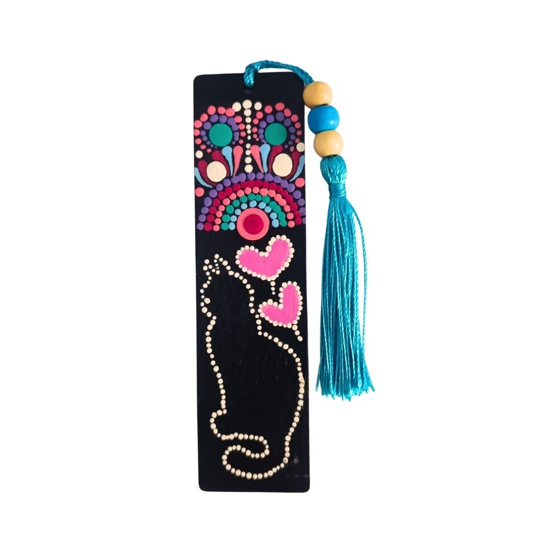 Separador de libros de madera negra con diseño de gato, mandala, y dos corazones rosas. Termina con una borla de hilo azul turquesa atada con cuentas.