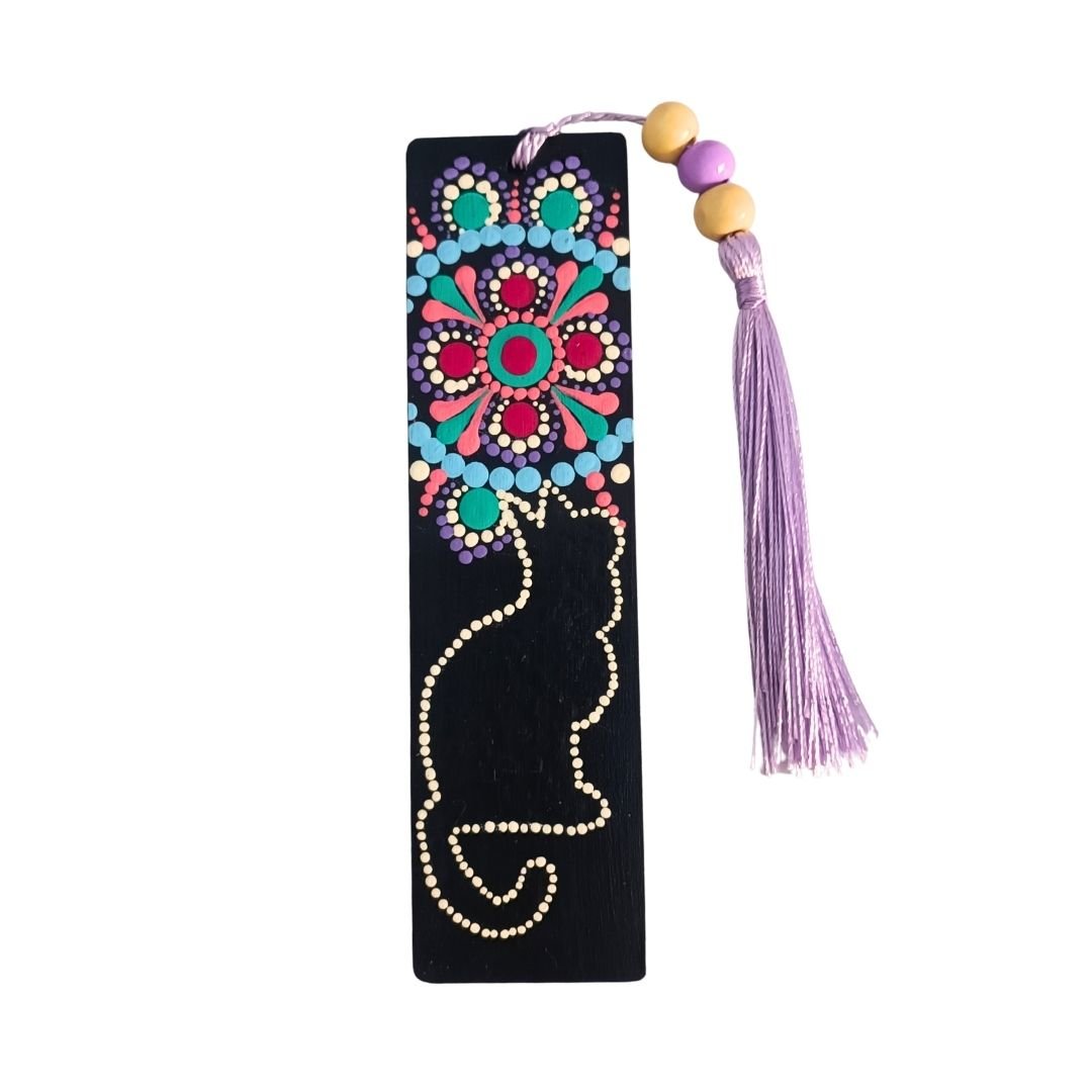 Separador de libros de madera negra con diseño de gato y un mandala floral, y una borla de hilo lila o lavanda atada con cuentas de madera.