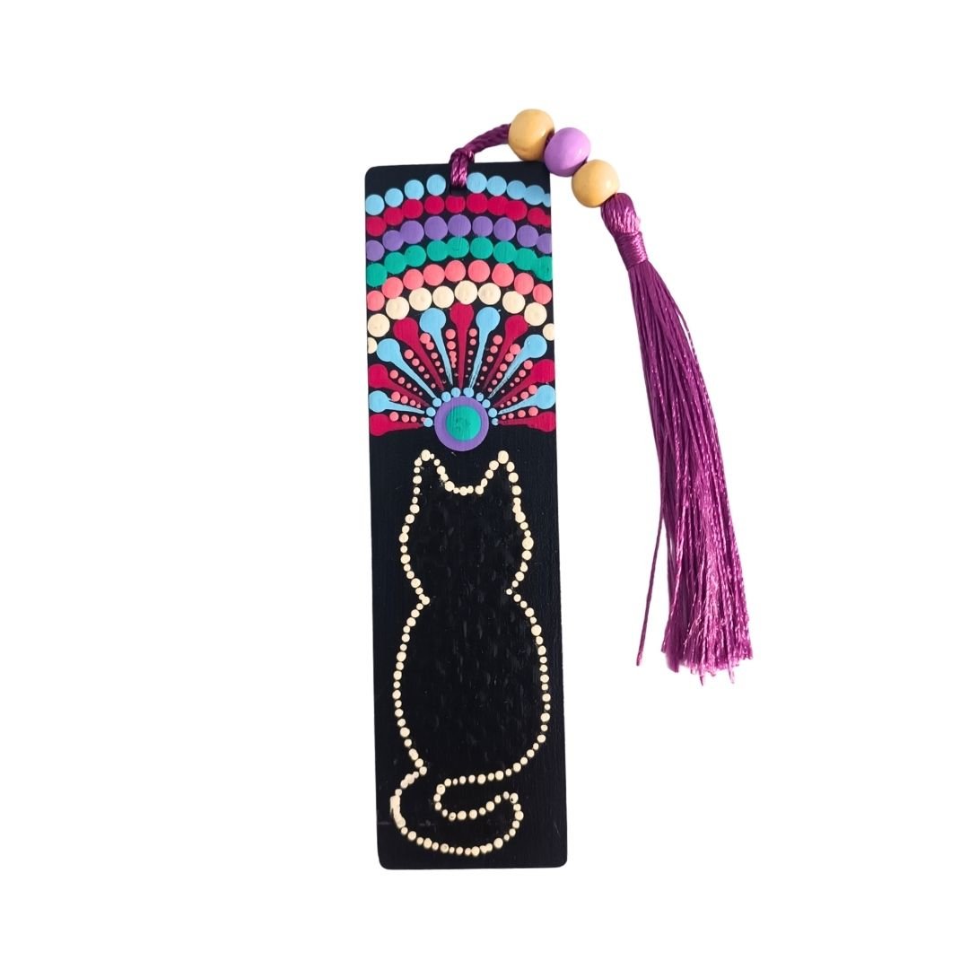 Separador de libros de madera negra con diseño de gato y mandala en tonos cálidos y frÃos, y una borla de hilo magenta o fucsia atada con cuentas.
